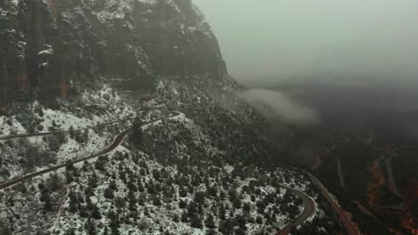 aerial descending shot showcasing a long snow covered road snaking through the red rock mountains of zion national park