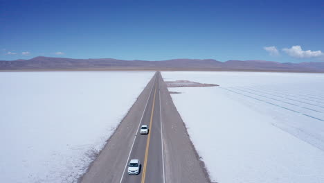 Los-Coches-Conducen-Por-Una-Carretera-Recta-A-Través-De-Salinas-En-Argentina,-Antena