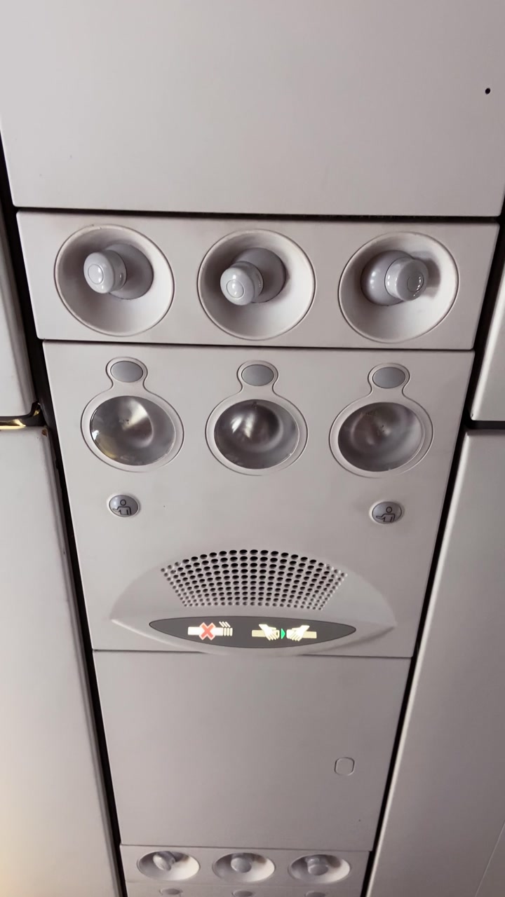 POV plane overhead panel ugc style vertical video during flight in air. Travel vlogger inside aircraft. Seatbelt sign and no smoking light on. Flying in commercial airline trip during daytime