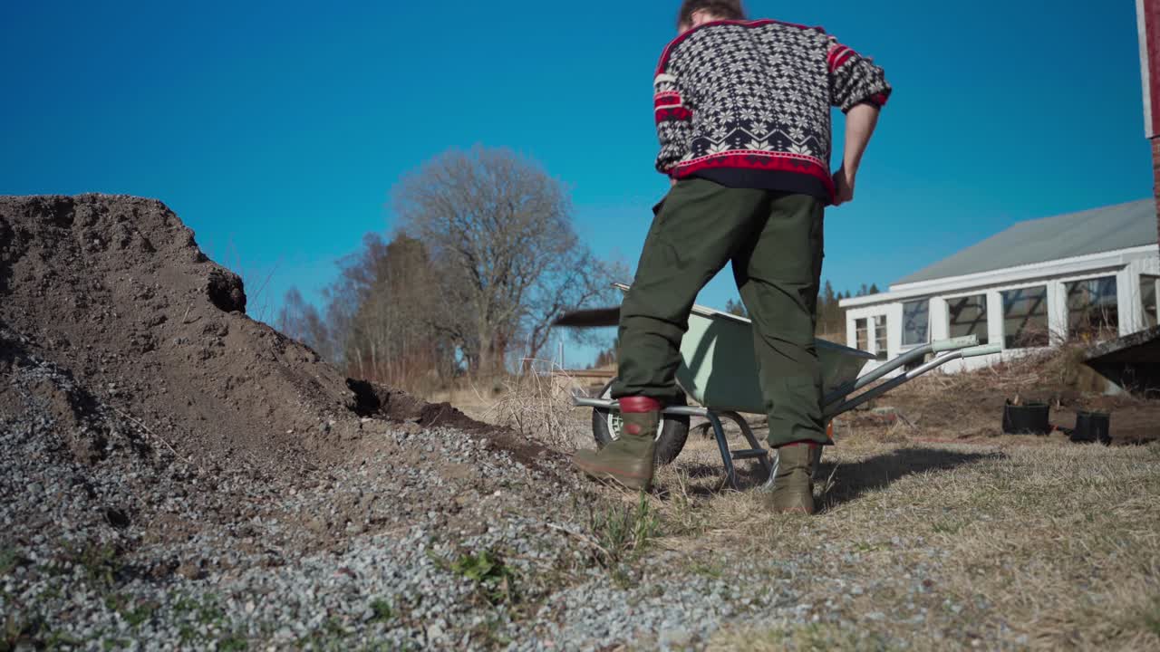 Man Shoveling Soil Into Wheelbarrow At Farm In Indre Fosen, Norway