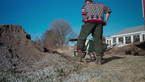 man shoveling soil into wheelbarrow at farm in indre fosen, norway