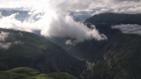 high white clouds move slowly over the winding road and river in the valley between the high green mountains in the hardangervidda national park in norway