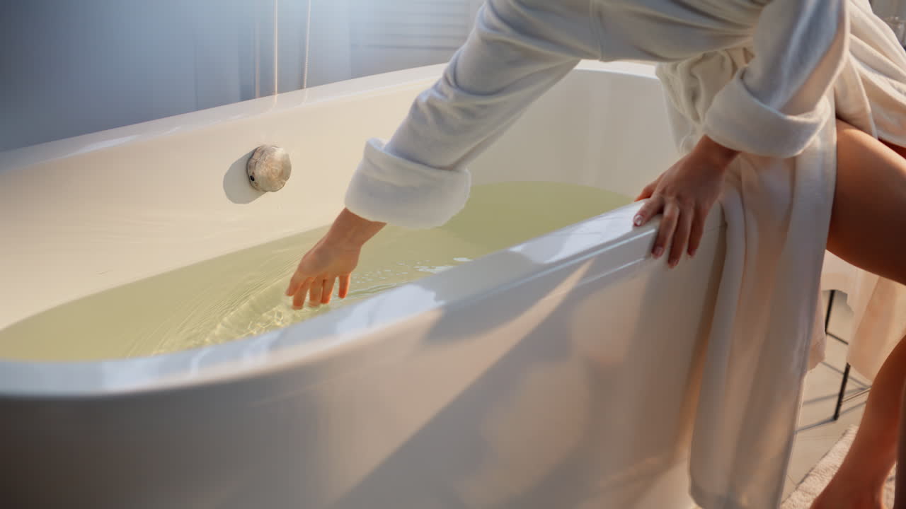 Primo piano di mano che prova l'acqua della vasca preparando la spa. Donna elegante che verifica la temperatura