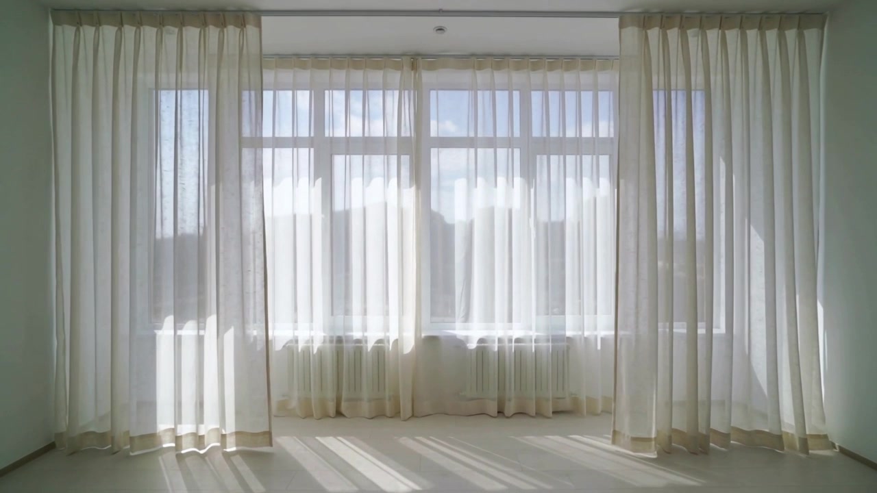 Cortinas transparentes moviéndose por la luz del sol y la brisa que entra por la ventana de una habitación vacía, con las bandas en movimiento.