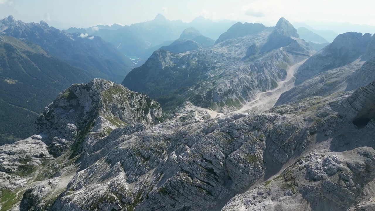 Rekaman drone udara Monte Canin di Friuli, Italia: puncak batu kapur yang terjal, punggung bukit berbatu, dan medan pegunungan Alpen yang dramatis di bawah langit cerah. Ideal untuk proyek alam, perjalanan, dan luar ruangan.