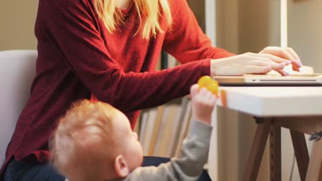 Mother-using-laptop-while-baby-standing-next-to-her-4k