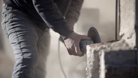 laborer on dusty construction site cutting concrete with angle grinder, front view