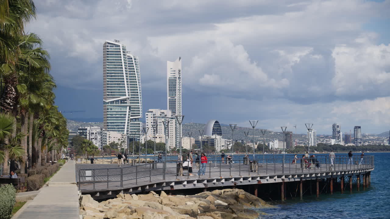 Limassol, Cipro - 26 febbraio 2026: Pontile di legno che si estende nel Mar Mediterraneo a Limassol con persone che camminano e moderni edifici a molti piani sullo sfondo.