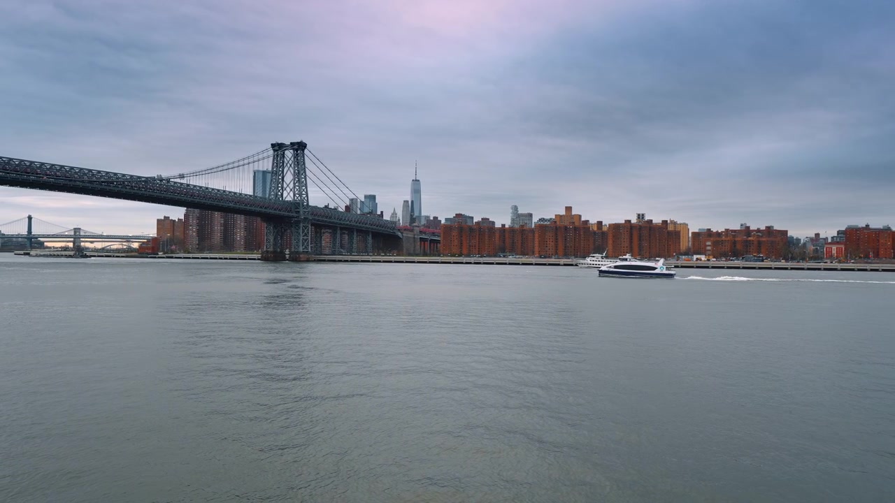 Ponte di Williamsburg, traghetto, East River, crepuscolo, skyline di New York. Ponte di Williamsburg con lo skyline di Manhattan al crepuscolo, traghetto di New York che passa, acqua calma dell'East River, cielo coperto rosa-blu, vista da Brooklyn