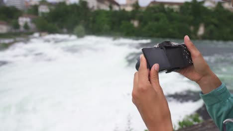 a person taking a photo of a waterfall in norway with a camera in hand