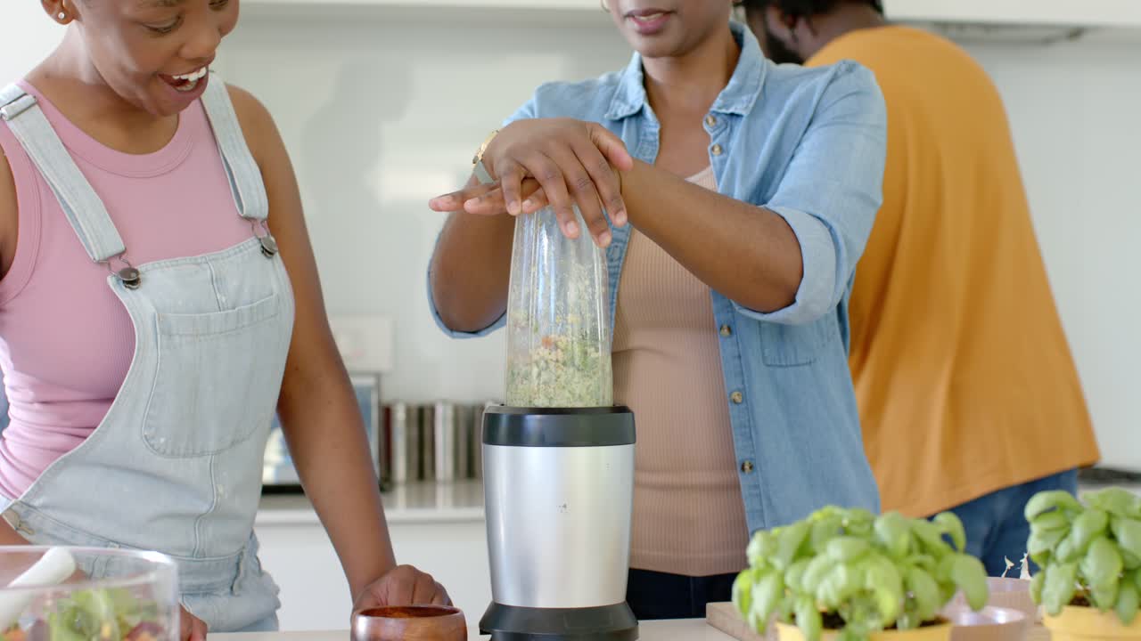 Keluarga Afrika-Amerika menekan wadah blender bening ke bawah, memblender campuran hijau di meja dapur.