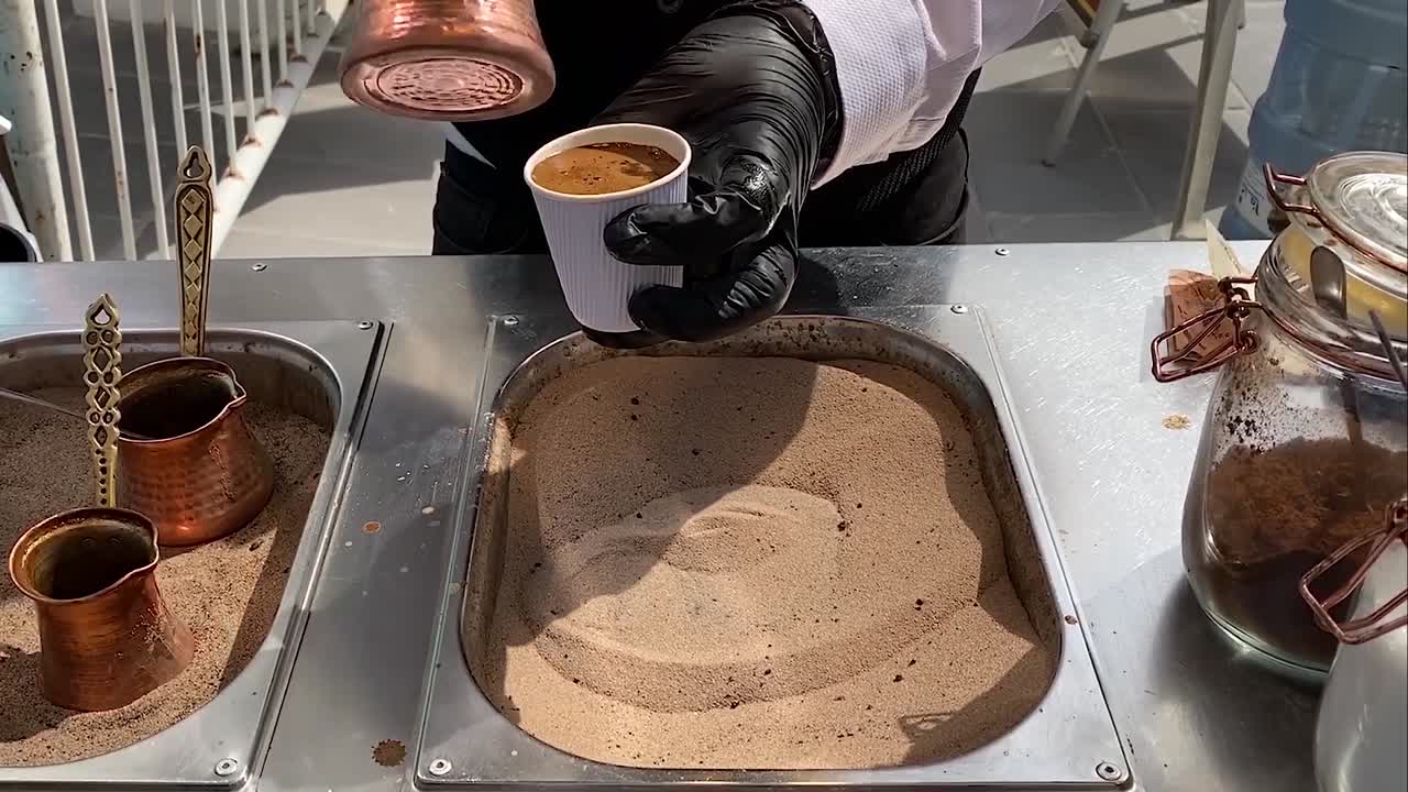 Man making Turkish coffee, using the iron cup drawing circles in the hot sand in Souq Asiri, Qatar