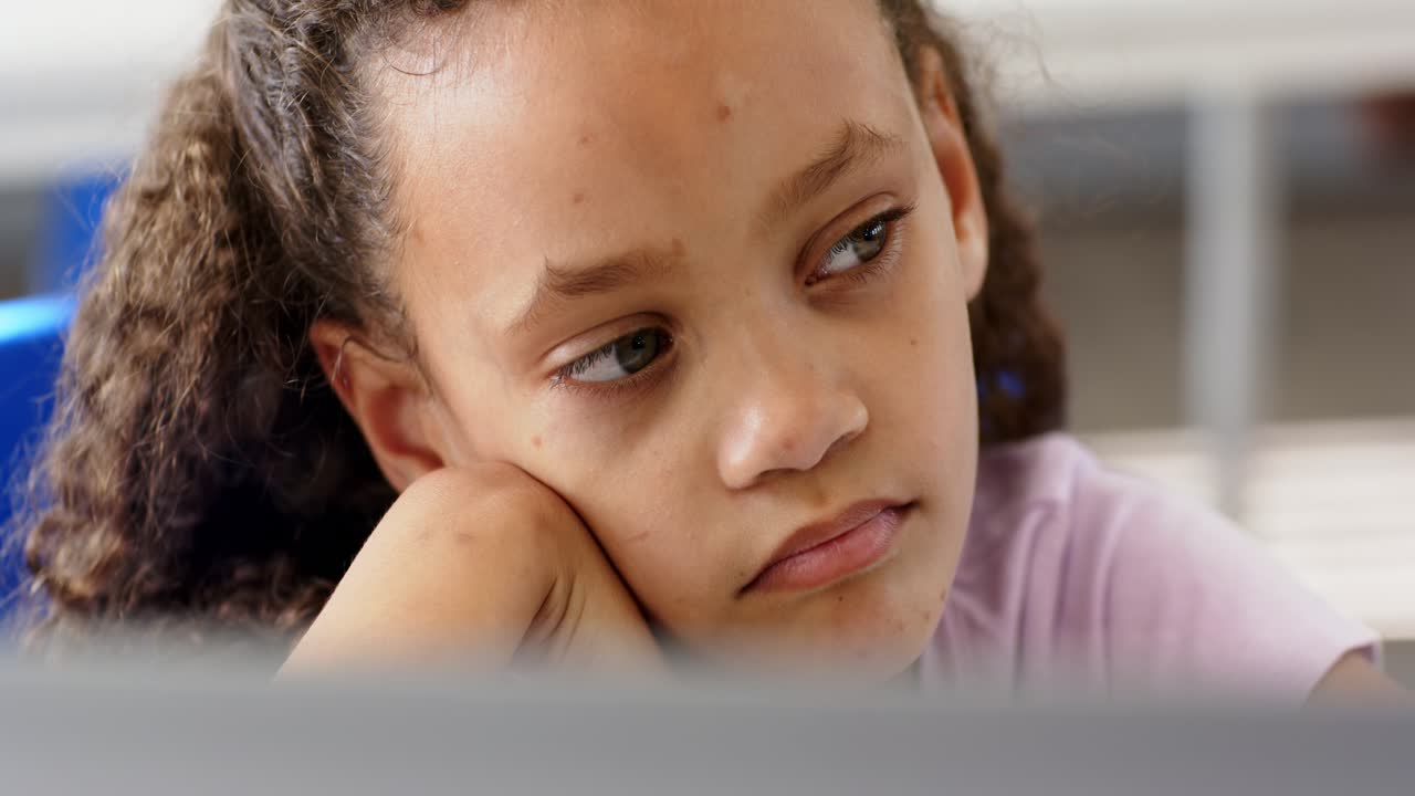 Ragazza afroamericana adolescente con la guancia appoggiata sulla mano, guarda a destra, pensa, bordo della scrivania sedia blu