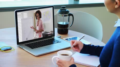 Caucasian-female-student-using-laptop-on-video-call-with-female-teacher,-making-notes