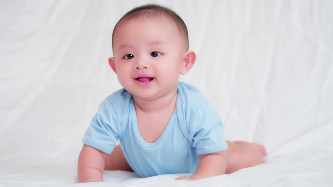 Happy family, Cute Asian newborn baby wear blue shirt lying, crawling play on bed looking at camera with laugh smile happy face.