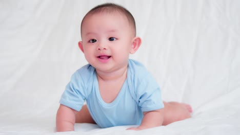 happy family, cute asian newborn baby wear blue shirt lying, crawling play on bed looking at camera with laugh smile happy face.