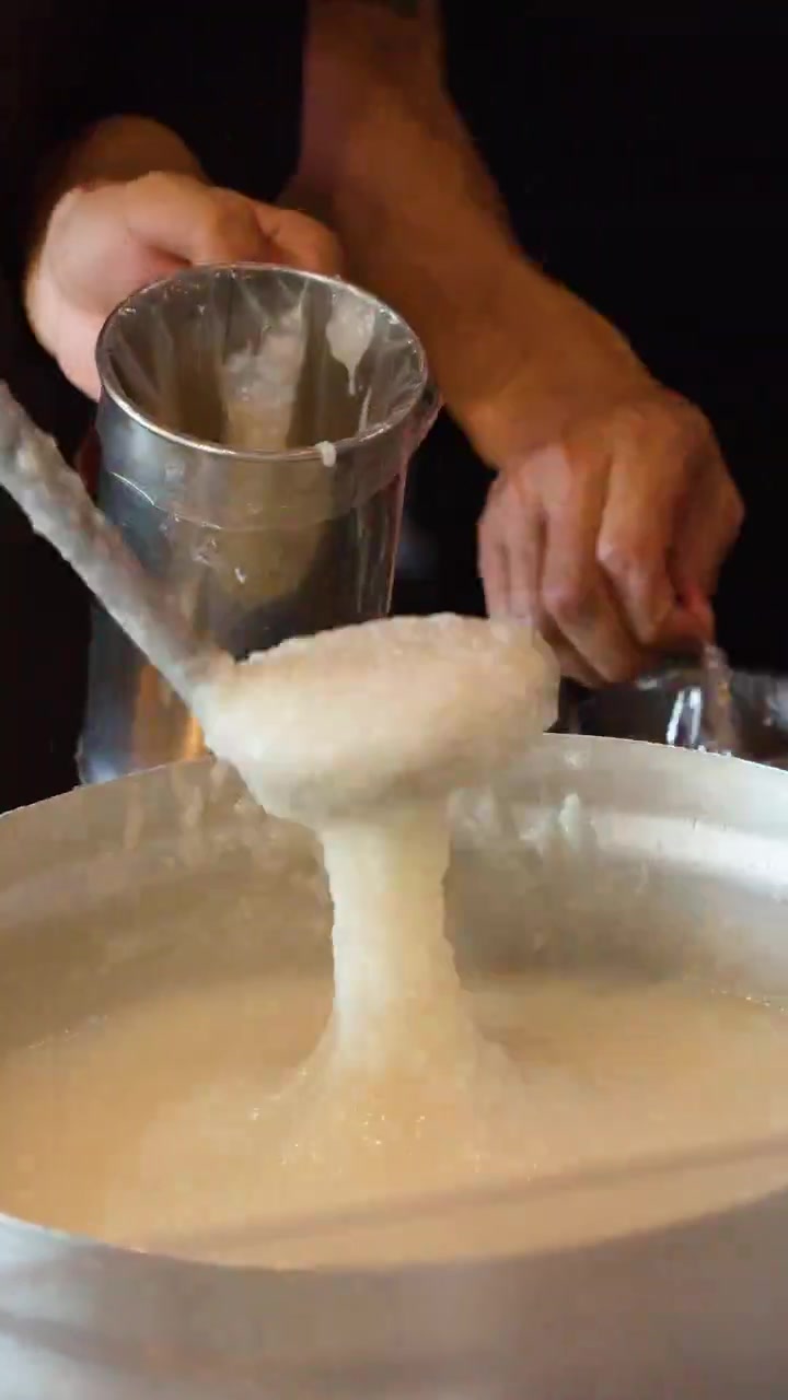Primo piano di uno chef che serve congee caldo da una grande pentola di metallo in sacchetti da asporto.