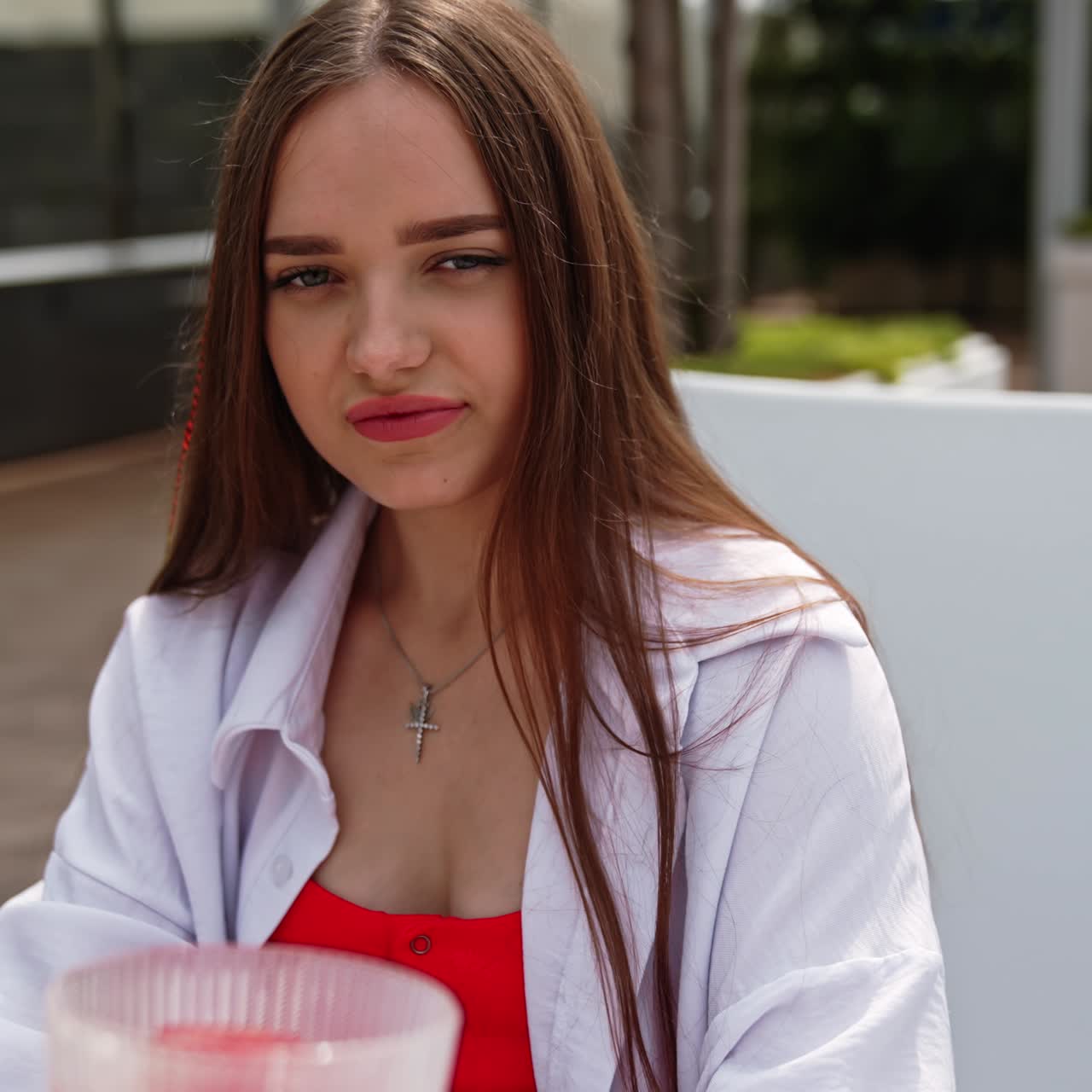 Lovely brunette sitting on deckchair drinking cocktail. Young lady spending time outdoors in spa near the swimming pool. Close up