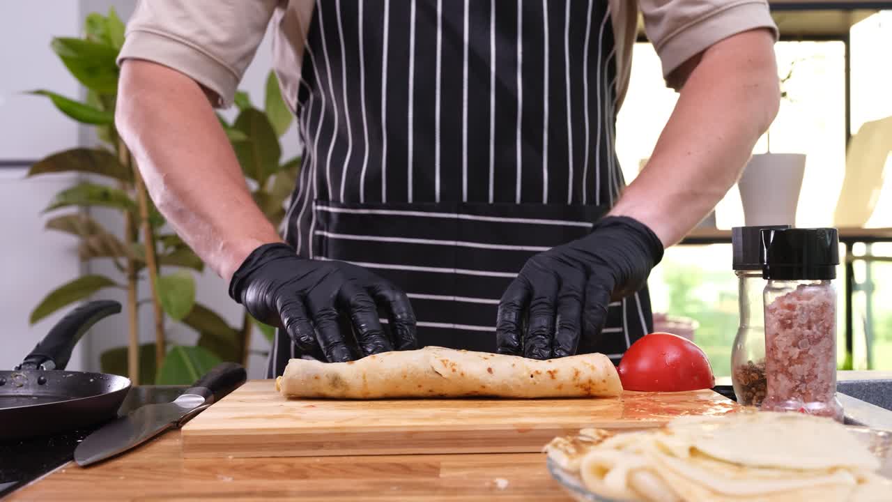 Cuoco assembla un wrap di shawarma affettando il rotolo con il coltello.