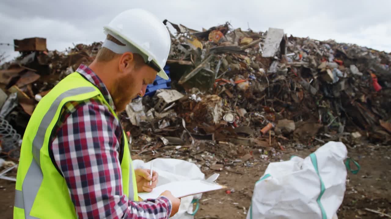 trabajador masculino escribiendo en el clipboard en el depósito de chatarra 4k