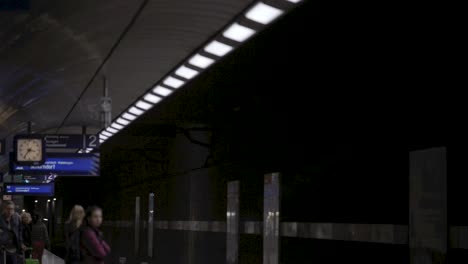 commuters wait on a dimly lit underground platform as a train arrives