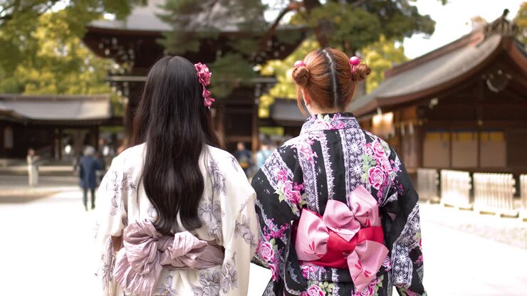 Vista posteriore di due donne in kimono floreali che camminano e si inchinano in un santuario giapponese