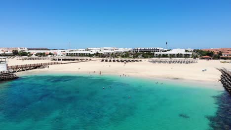 Aerial-View-Of-Lush-Blue-Turquoise-Ocean-Waters-Beside-Bikini-Beach-With-View-Of-Resorts-And-Villas-In-Background