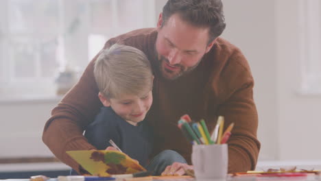 padre con hijo en casa haciendo artesanía y haciendo imágenes de hojas en la cocina