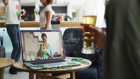 smiling african american woman with beer wearing clover shape band on video call on laptop