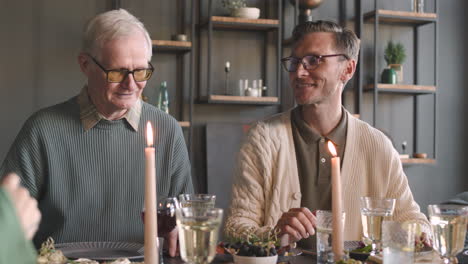 portrait of two multigenerational men sitting at dinner table and talking with family during a reunion at home