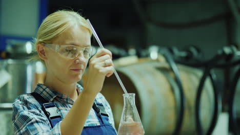 female researcher working with product samples in a flask against the background of wooden barrels o