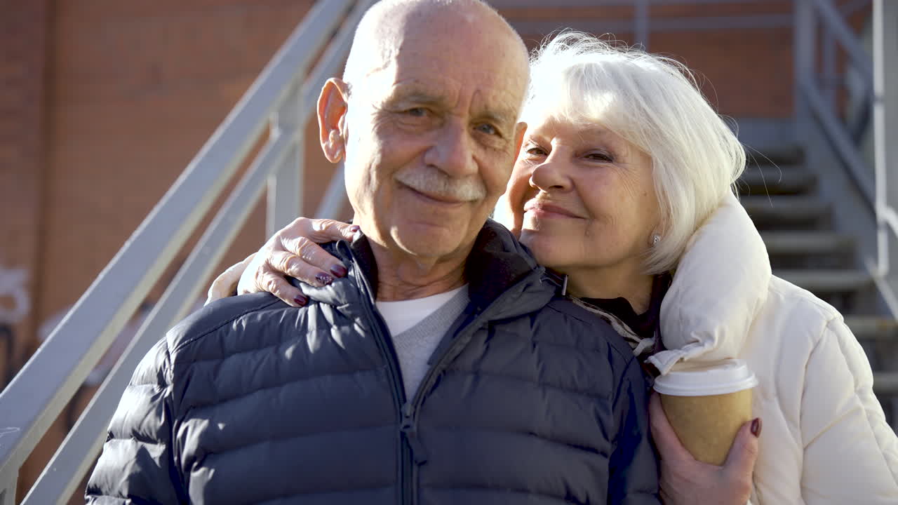 Close-up view of a senior couple hugging and looking at camera in the street on a winter day