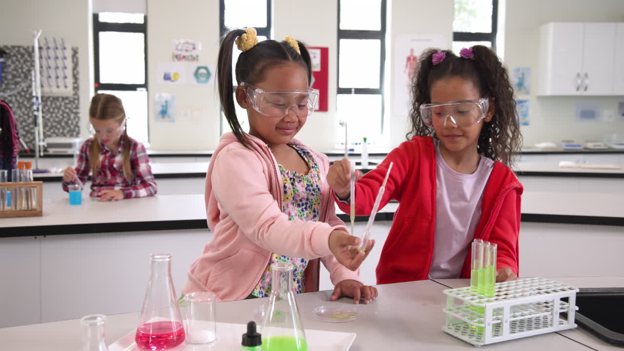 In school, diverse girls wearing goggles conducting science experiment with test tubes