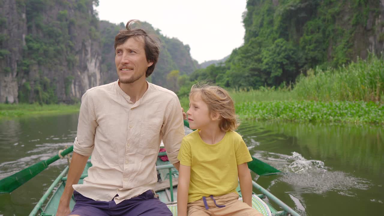 Seorang pria muda dan putranya di atas perahu melakukan perjalanan sungai di antara bebatuan kapur yang spektakuler di Ninh Binh, sebuah tujuan wisata di Vietnam utara. Konsep perjalanan ke Vietnam