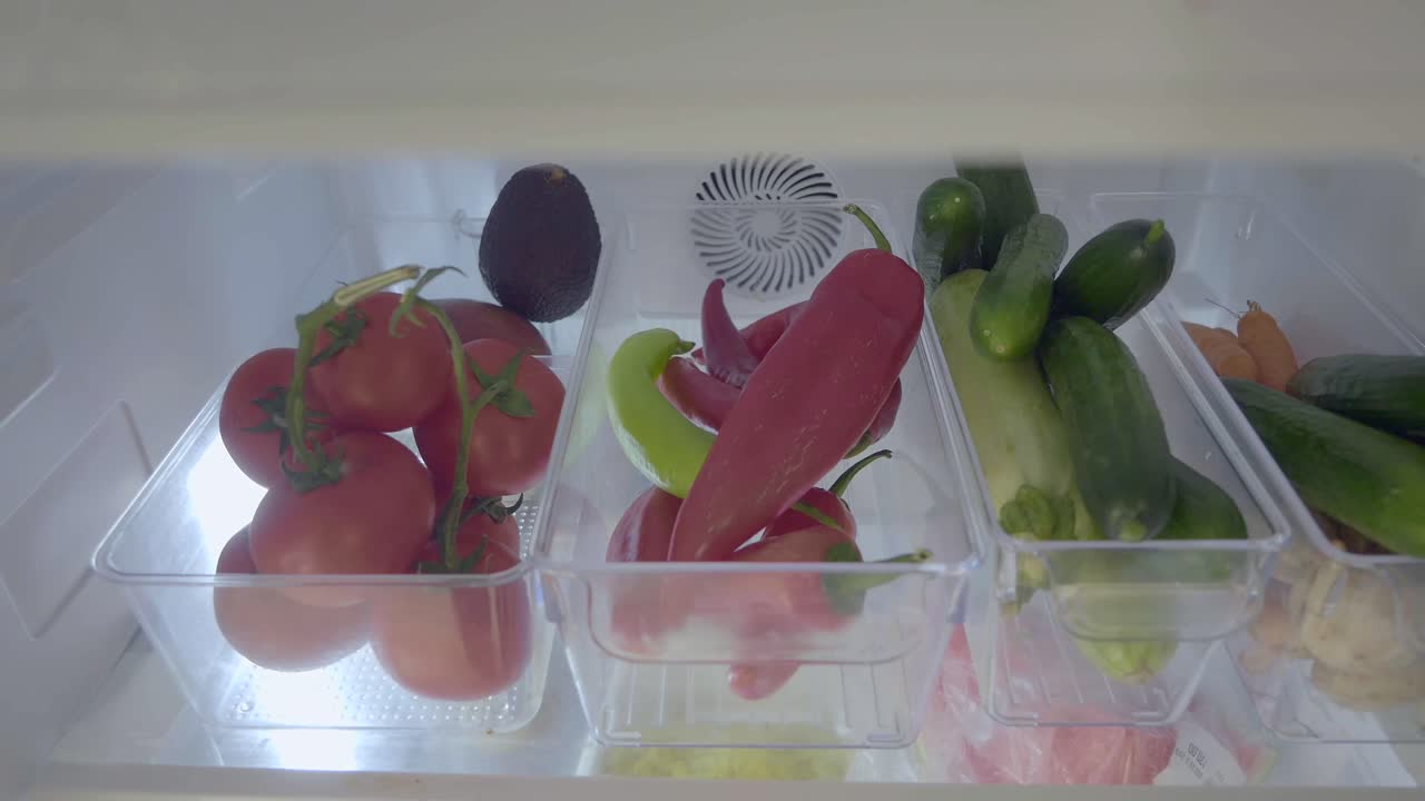 Hand taking a red pepper from an organized refrigerator