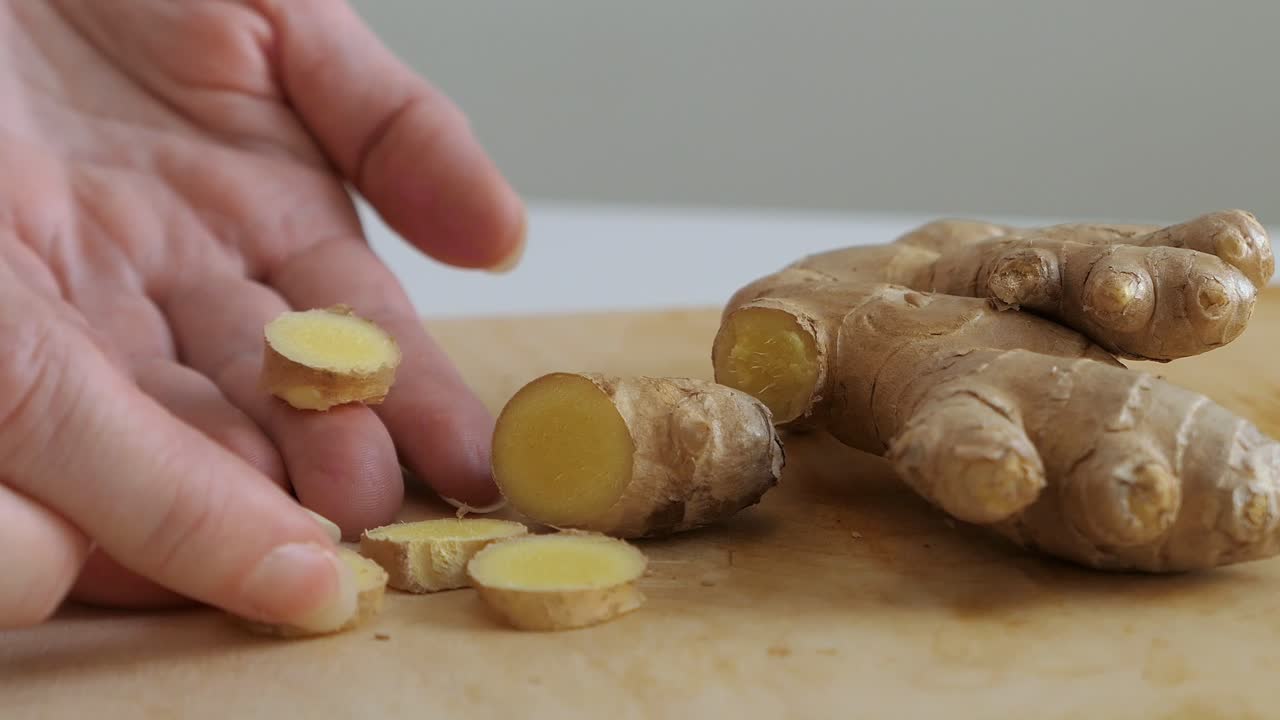 Woman picking up fresh ginger slices from wooden cutting board, healthy eating, close up