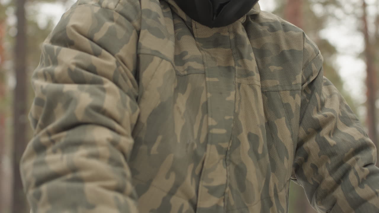 Piloto de quadriciclo branco em floresta nevada segurando o acelerador e o guidão, vestindo jaqueta camuflada e viseira de capacete reflexiva. Retrato em close-up mostra o homem focado firmando a mão enluvada na manopla, com poeira de neve na luva.