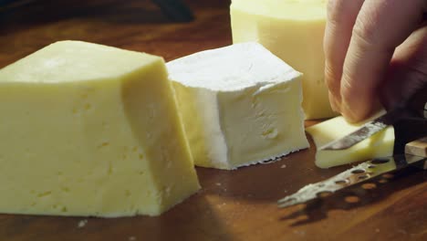 three cheese blocks on cutting board: wedge of gouda cheese is sliced