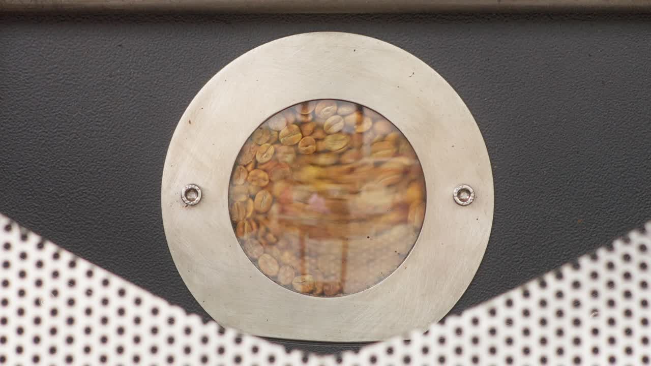 Coffee beans tumbling behind a round roaster window, centered industrial closeup