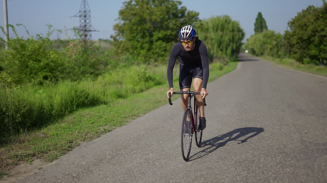 Primo piano di un ciclista uomo con casco che pedala lungo il percorso, prendendo velocità.