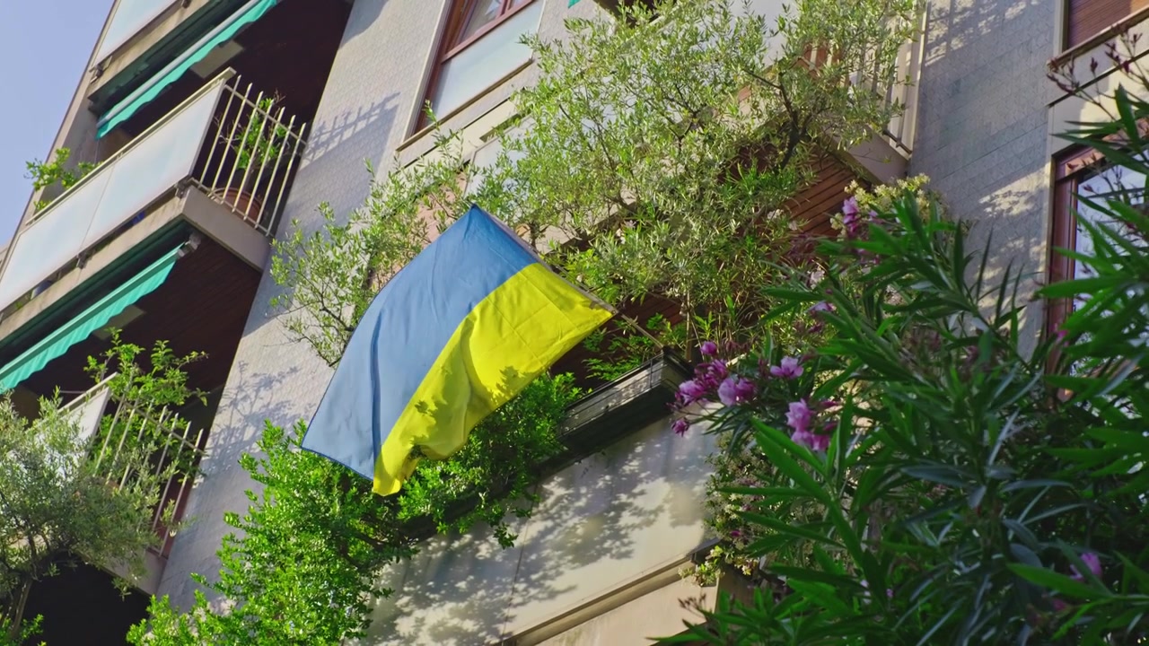 Una bandiera nazionale ucraina esposta da un balcone di un edificio residenziale a Milano, che simboleggia solidarietà e supporto in un quartiere urbano.