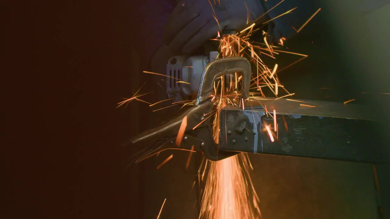 Angle grinder sparks foreground framing effect, handheld close up shot. Blacksmith cutting metal seen through a workshop tool blur making bright fiery shower.