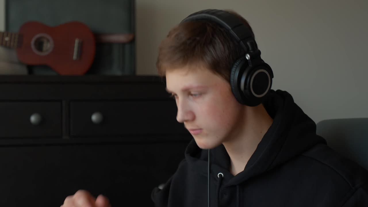 Person i sort hættetrøje sidder indendørs, rolig stemning, ukulele på kommoden