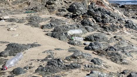 desechos marinos de plástico esparcidos por la costa rocosa y arenosa.
