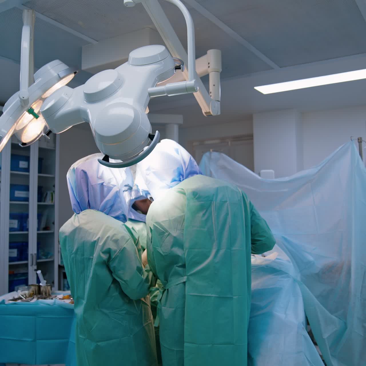 Cooperating orthopedics perform surgical operation. Doctors wearing robes and protective helmets working at arthroscopic surgery