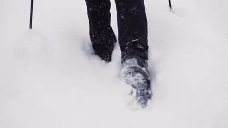 slow motion low angle shot of mountaineer with hiking poles stepping through deep snow in the mountains