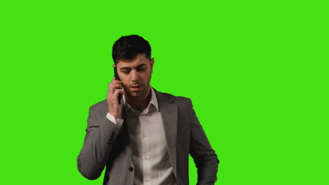 unhappy businessman wearing suit making call on mobile phone against green screen background