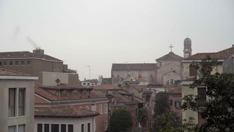a wide view of traditional venetian rooftops and the spires of historic churches under an overcast, hazy sky.