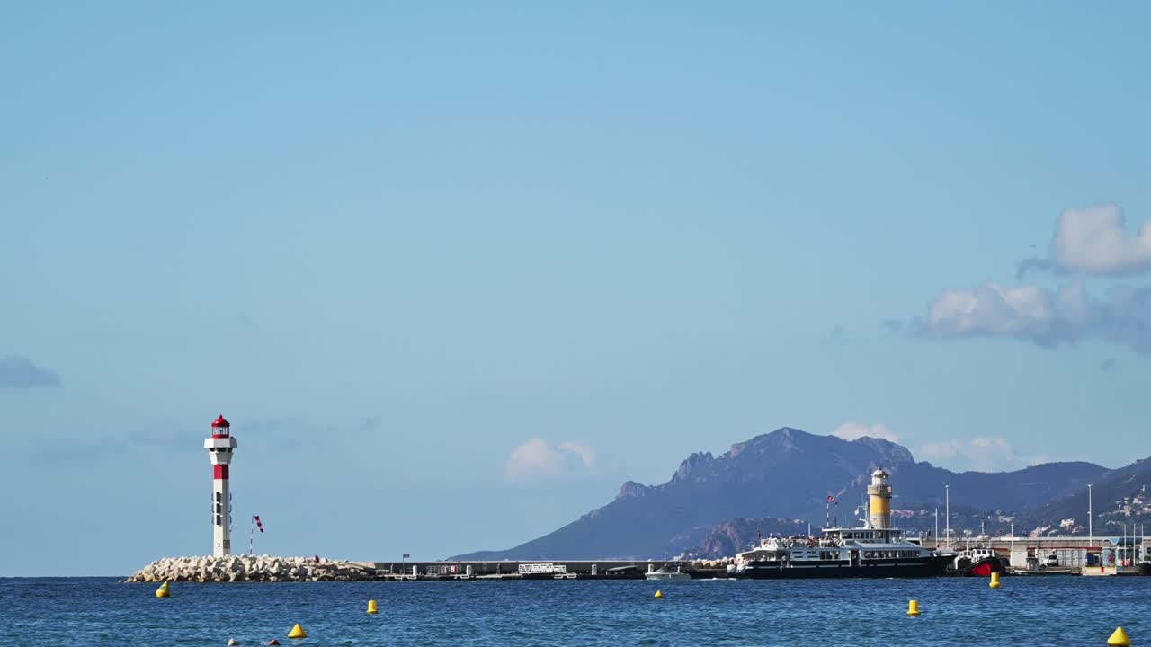 View of the sea port in Cannes, France. Lighthouse, floating boats, hills on the background