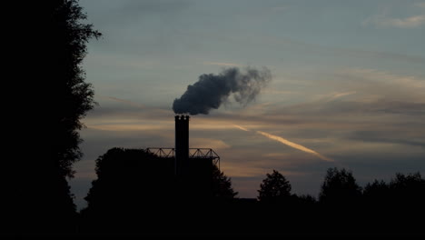 hermosa silueta de chimenea de fábrica humeante contra una puesta de sol en cámara lenta